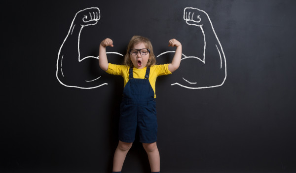 Child with muscled arms drawN on blackboard behind child