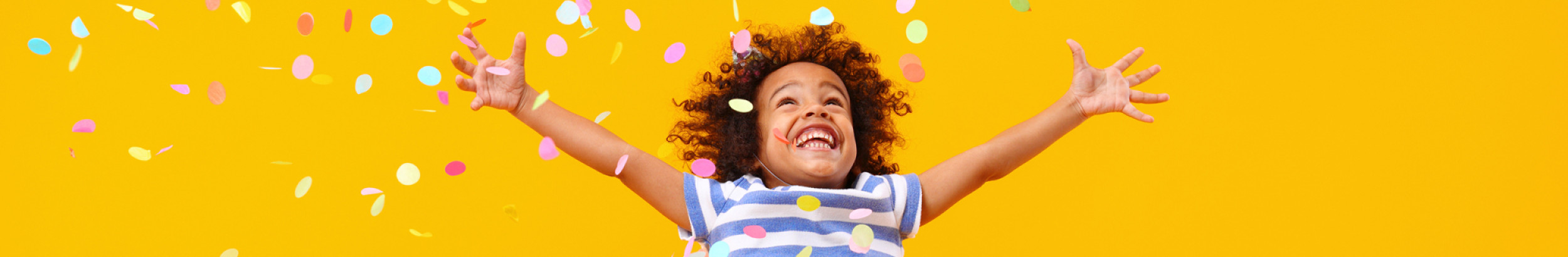 Young girl jumping with confetti and yellow background