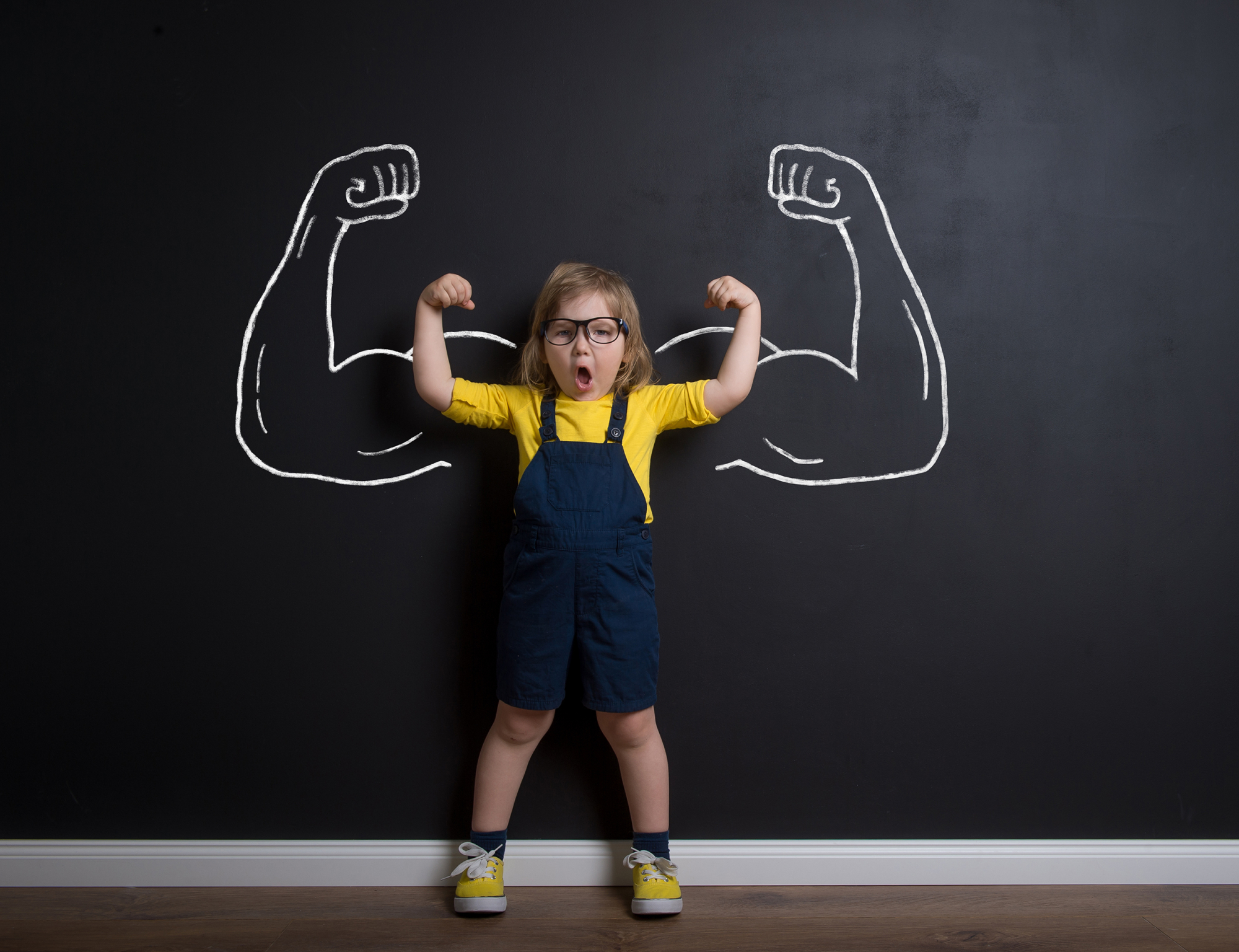 Child with muscled arms drawN on blackboard behind child